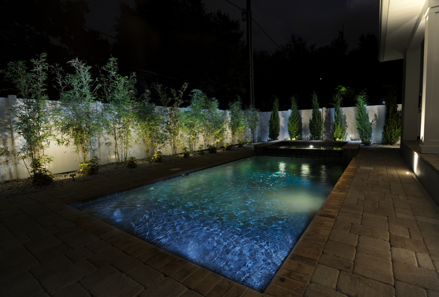 Landscape lighting around a residential pool and pathway at night