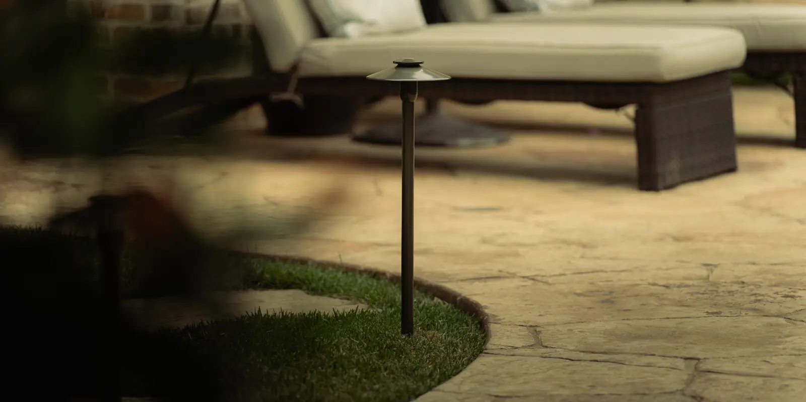 Solid brass path light installed at the edge of a flagstone patio