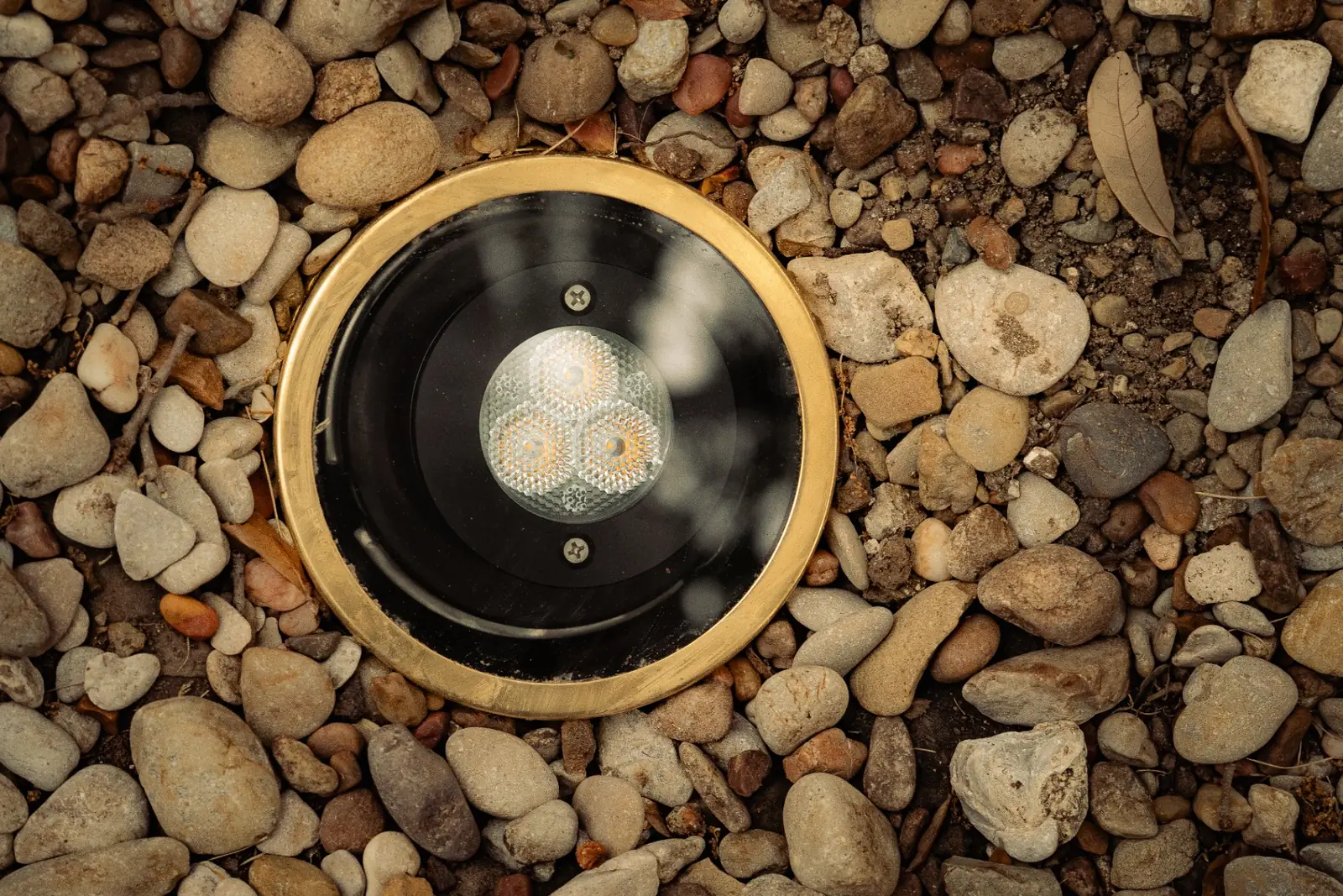Solid brass in-ground uplight fixture set in a river rock bed