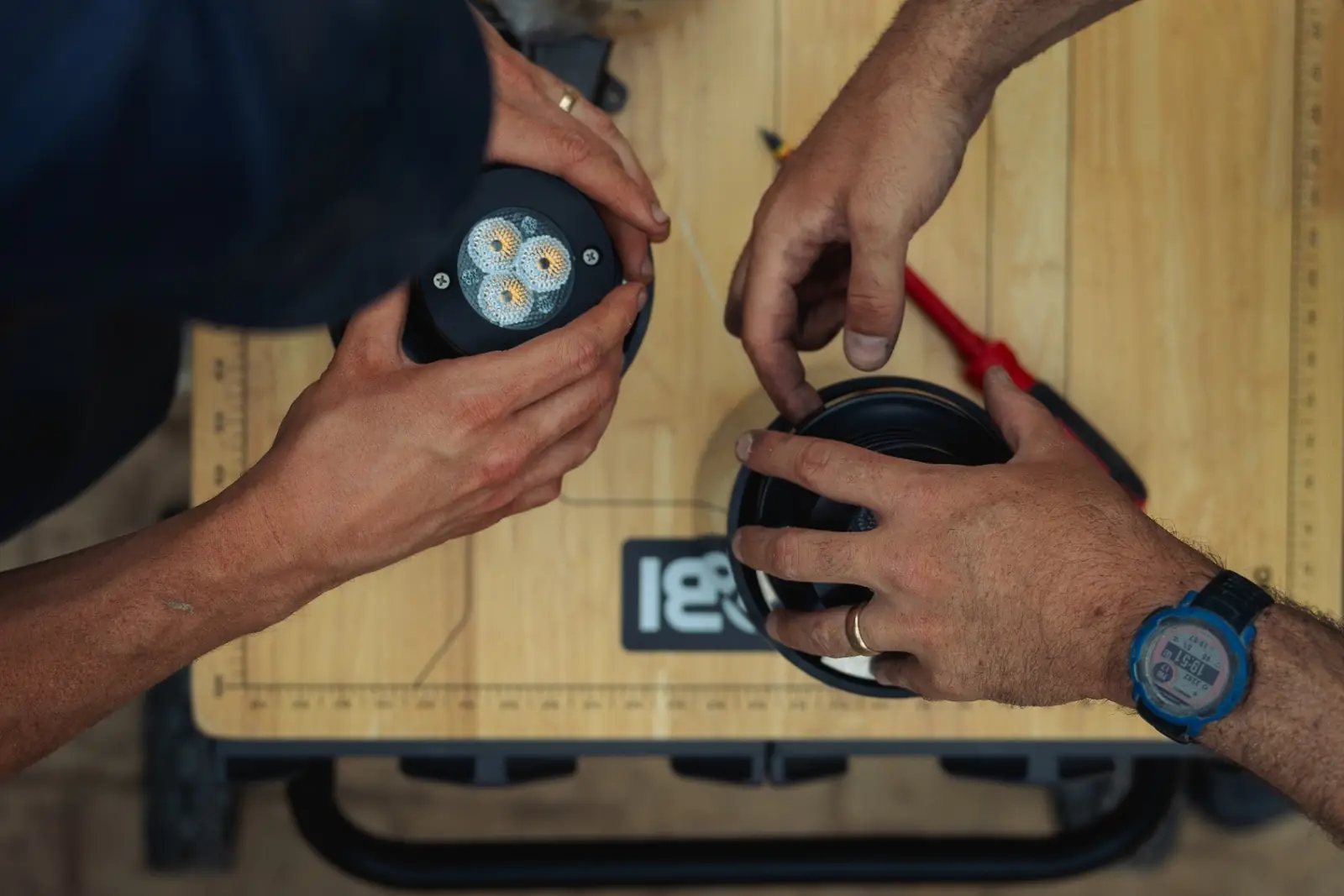 Hands assembling an LED spotlight fixture on a work bench