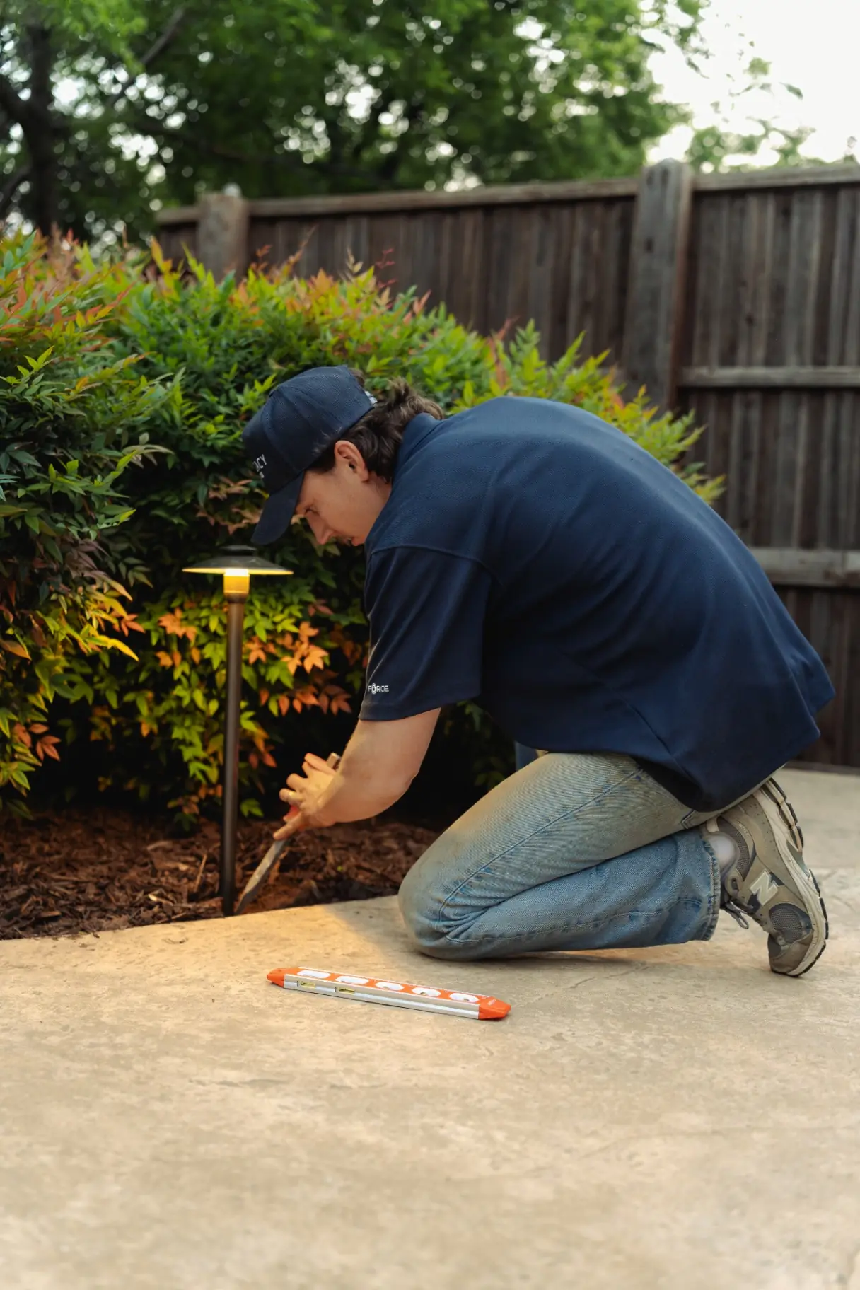 Technician installing and leveling a brass path light in a mulched bed